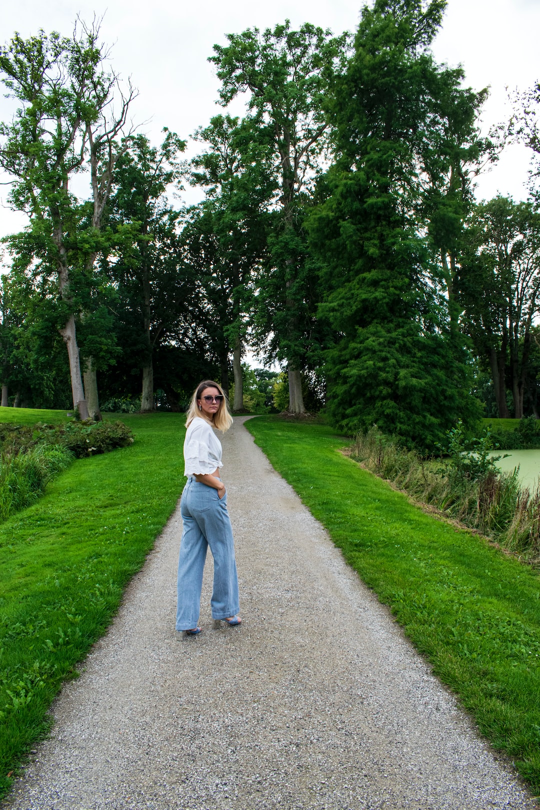 woman in white long sleeve shirt and blue denim jeans standing on gray asphalt road during