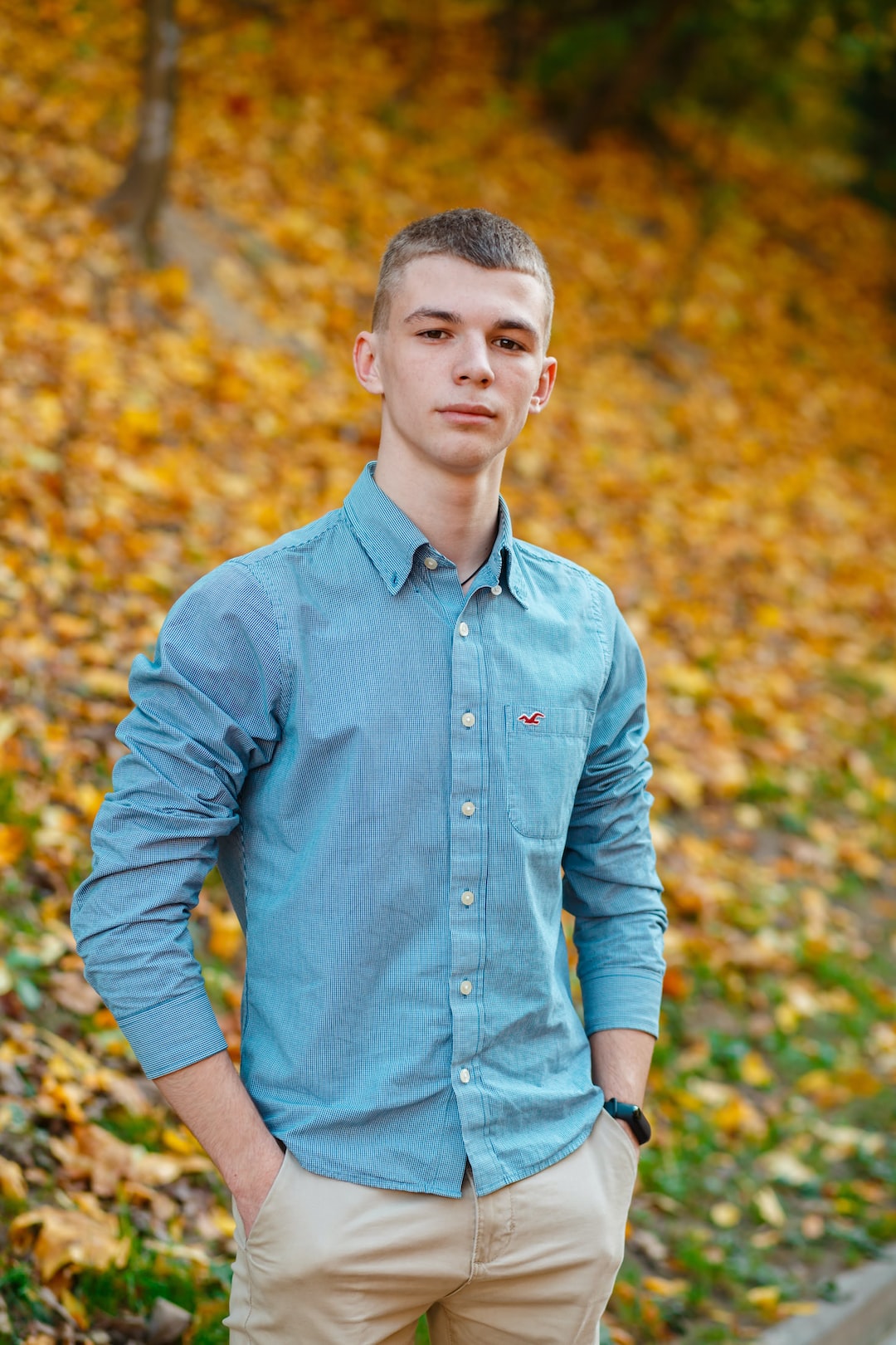 man in blue dress shirt standing near brown leaves during daytime