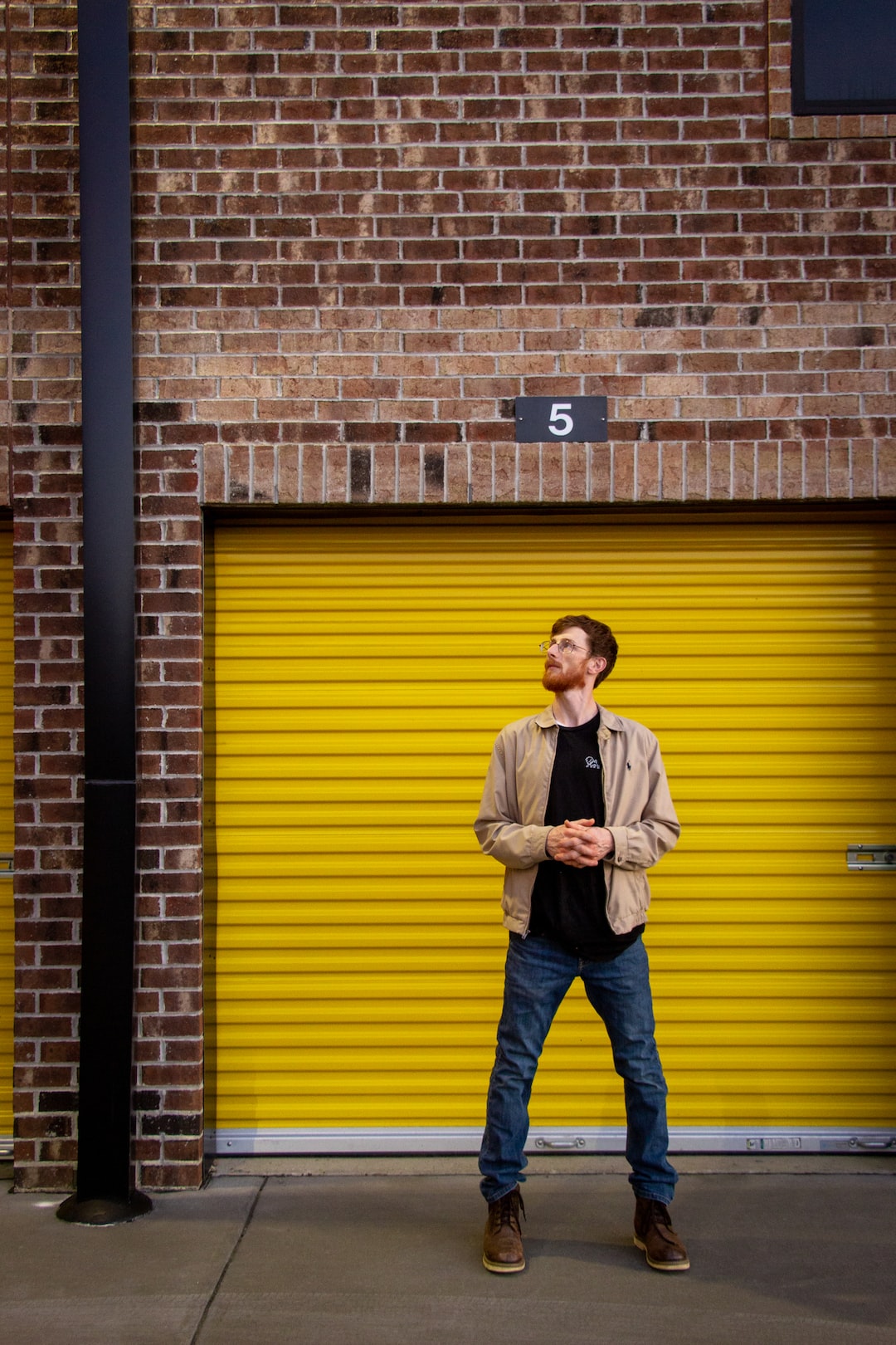 man in white dress shirt and blue denim jeans standing beside brown brick wall