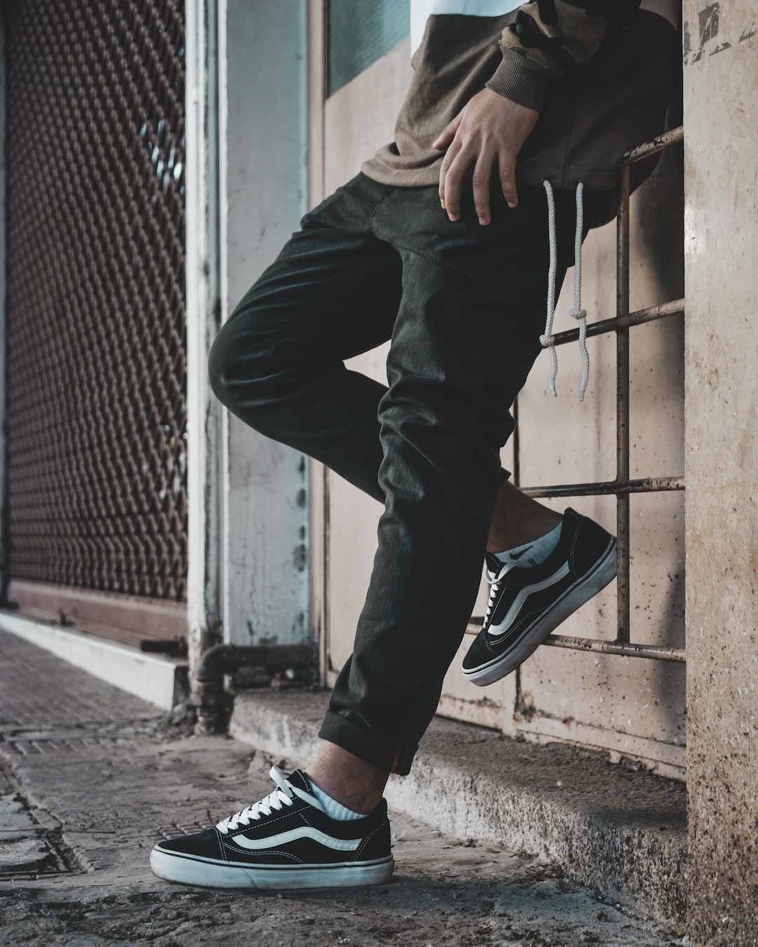 a man leaning against a wall wearing black and white sneakers