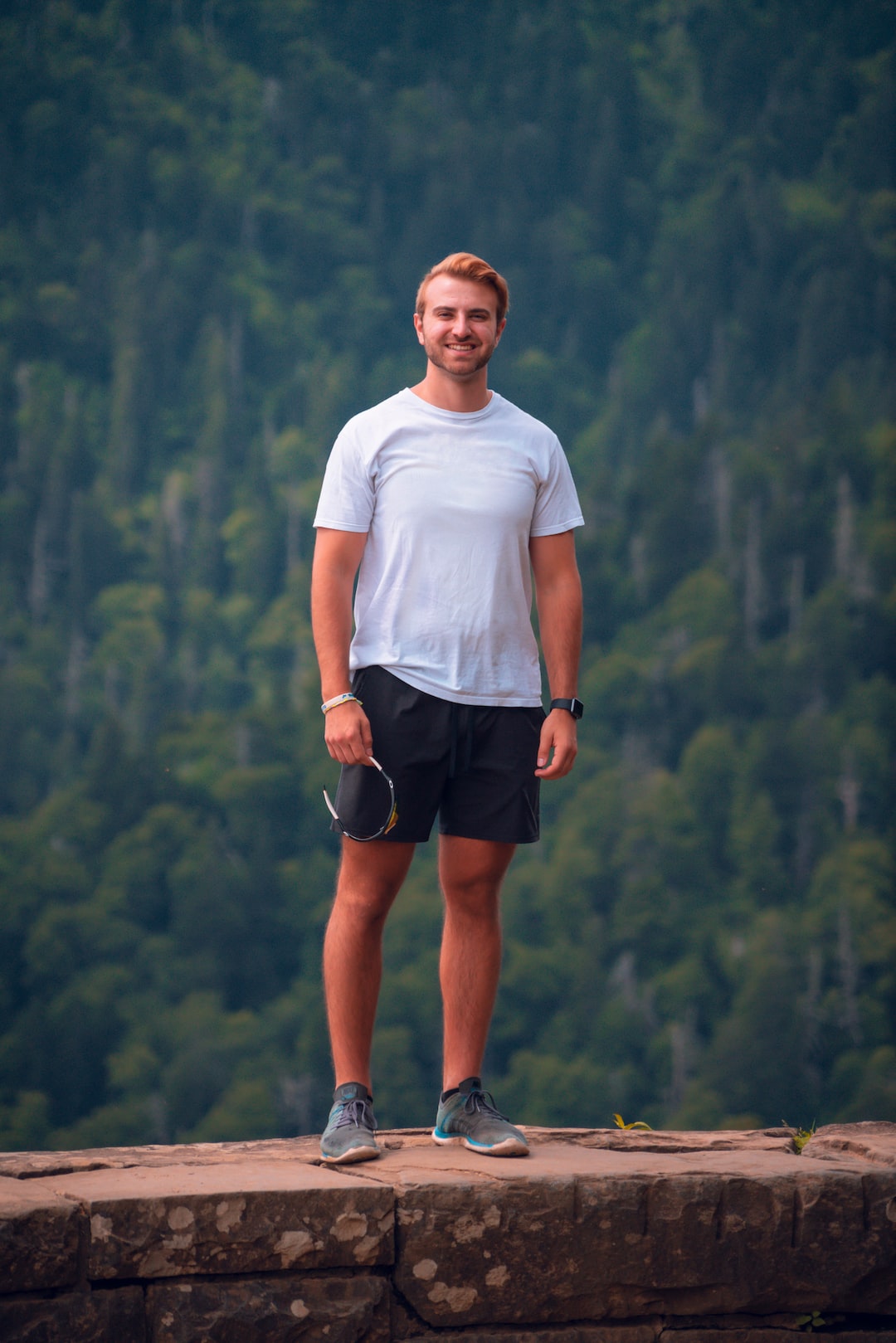 man in white crew neck t-shirt and black shorts standing on mountain during daytime