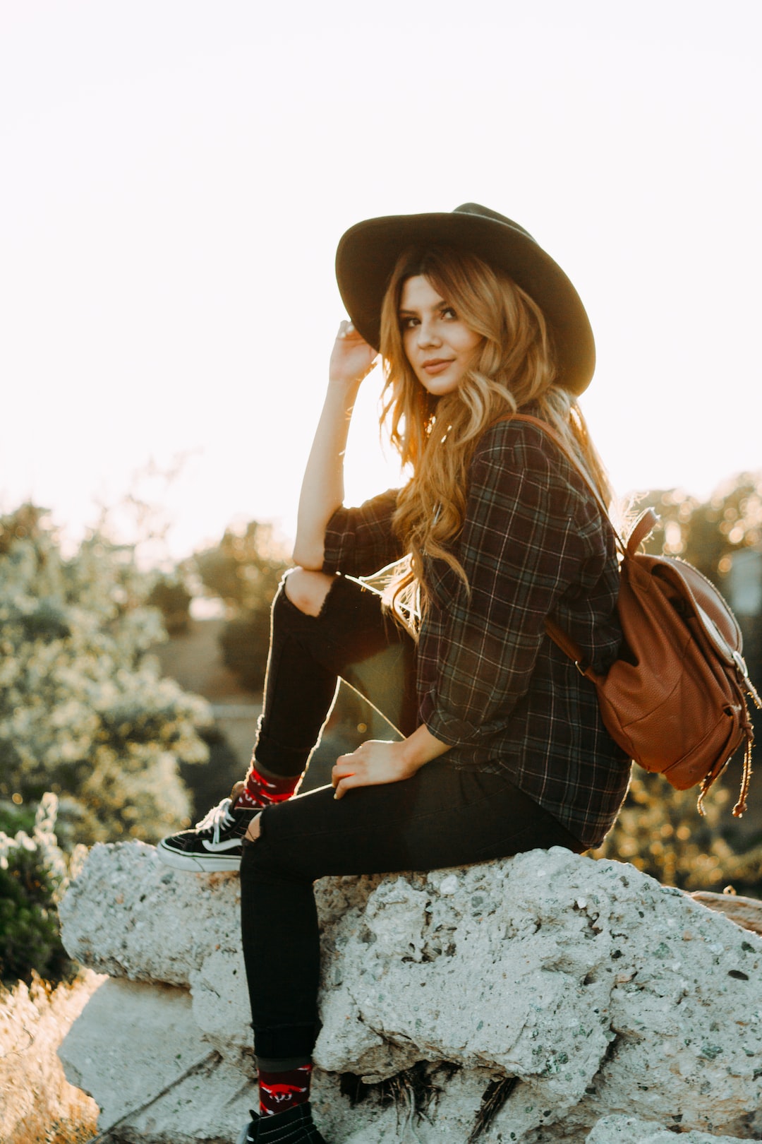 golden hour photography of woman sitting on rock while holding her hat