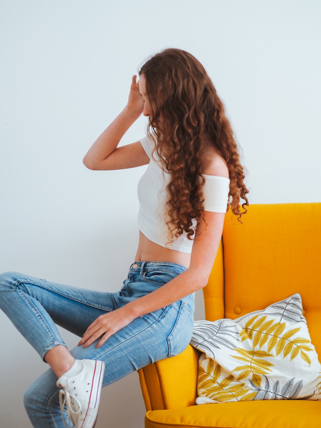 woman in white tank top and blue denim jeans sitting on yellow couch